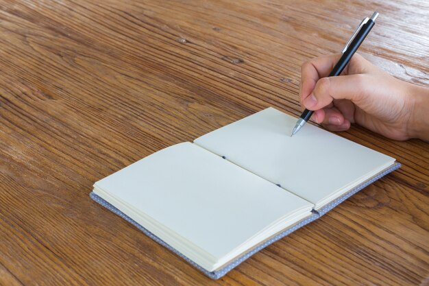 Hand hält einen Stift neben einem leeren Notizbuch