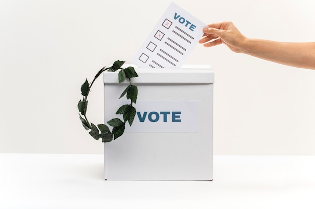 Hand legt Stimmzettel in Wahlbox und eine Krone