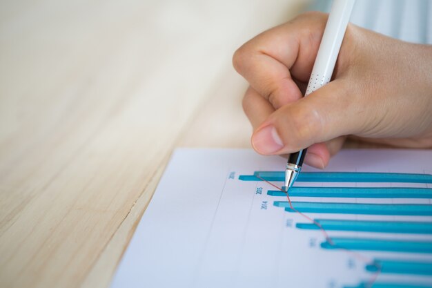 Hand mit einem Stift schriftlich auf einem Papier mit einem Balkendiagramm