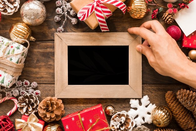 Hand mit Fotorahmen zwischen Weihnachtsdekorationen