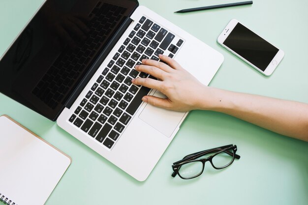 Hand mit Laptop in der Nähe von Smartphone und Brille