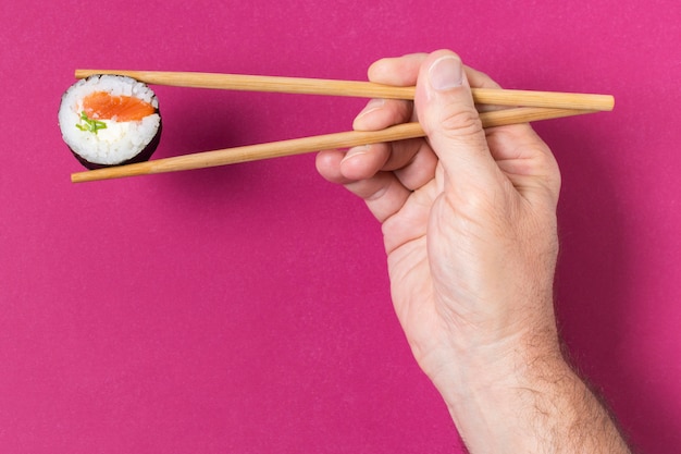 Hand mit Stäbchen und Sushi
