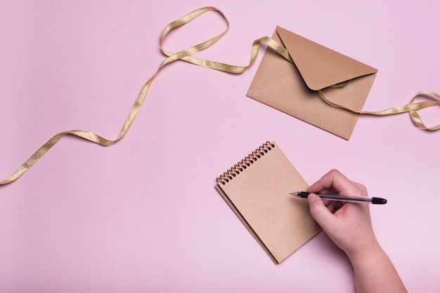 Hand mit Stift in der Nähe von Notebook, Umschlag und Farbband