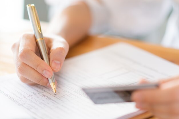 Hand mit Stift und Kreditkarte über Antragsformular.