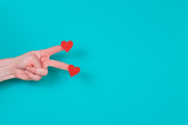 Hand mit zwei Fingern mit zwei Herzen auf einem blauen Hintergrund