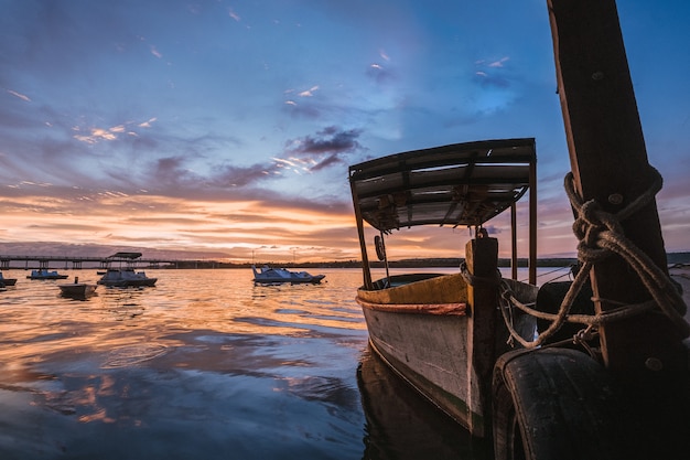 Handgemachtes Holzboot auf dem Meer unter einem bewölkten Himmel und Sonnenlicht während des Sonnenuntergangs