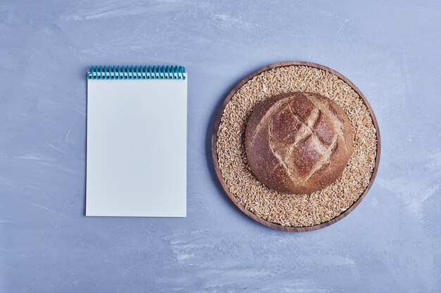 Handgemachtes rundes Brötchen auf grauem Tisch mit einem Rezeptbuch beiseite.