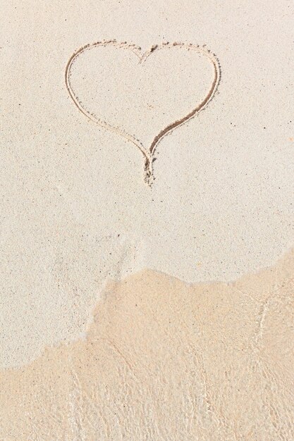 Handgeschriebenes Herz im Sand mit Welle, die sich im Strand nähert