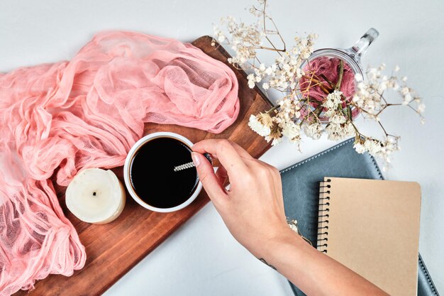 Handholdong eine Tasse Kaffee auf Holzbrett mit Kerze, Ponk-Tuch und Blumen.