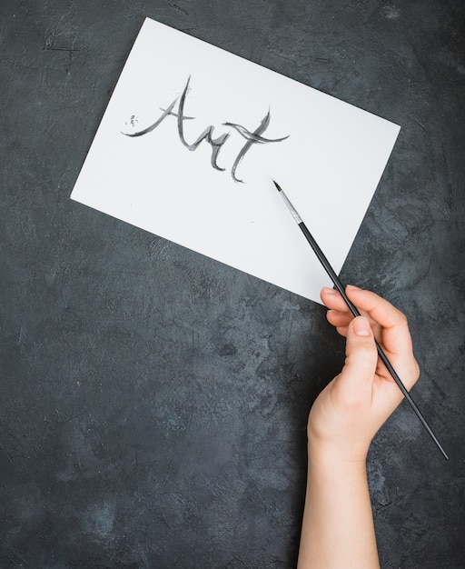 Kostenloses Foto handschriftlicher kunsttext der person mit malerpinsel auf papierblatt