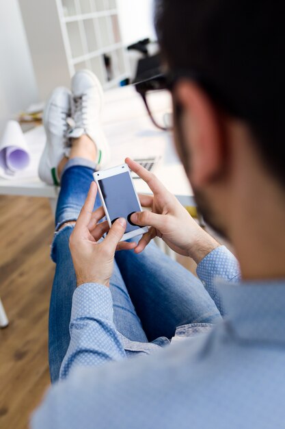 Handsome junge Mann mit seinem Handy im Büro.