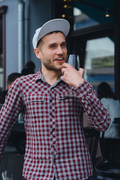 Handsome tätowierte Mann auf einer Sommerterrasse in einem Stadtcafé trinkt Wein. Straße Cafe.