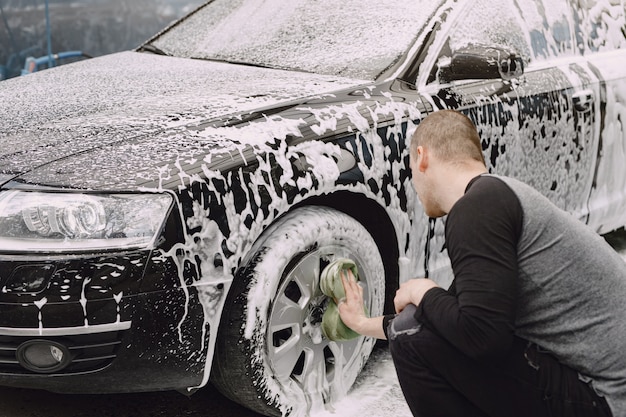 Handsomen Mann in einem schwarzen Pullover, der sein Auto wäscht