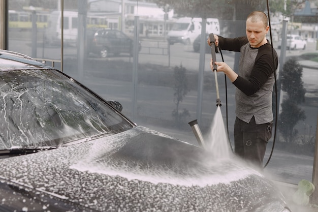 Handsomen Mann in einem schwarzen Pullover, der sein Auto wäscht