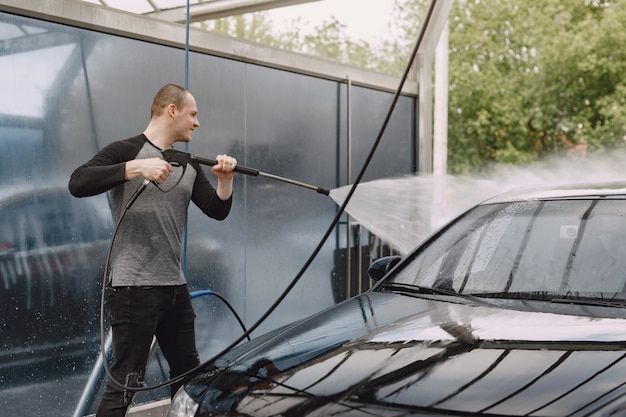 Handsomen Mann in einem schwarzen Pullover, der sein Auto wäscht