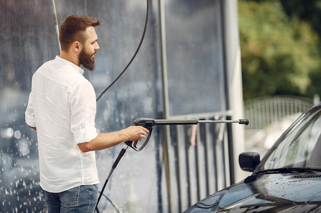 Handsomen Mann in einem weißen Hemd, das sein Auto wäscht