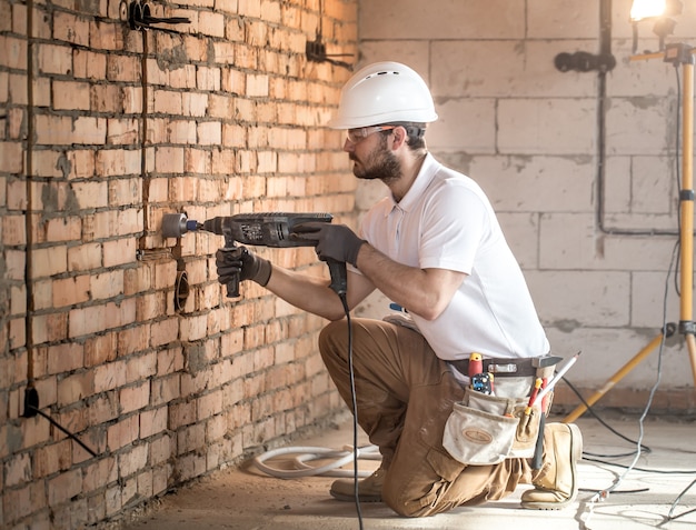 Handwerker verwendet Presslufthammer für die Installation, professionelle Arbeiter auf der Baustelle. Das Konzept des Elektrikers und Handwerkers.