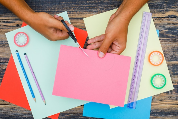 Handwerkliches Konzept mit Lineal, Bändern, Stiften auf hölzernem Hintergrund flach lag. Mann schneidet Papier.