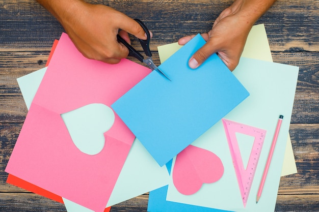 Handwerkskonzept mit Lineal, Bleistift auf hölzernem Hintergrund flach legen. Mann schneidet Papier.