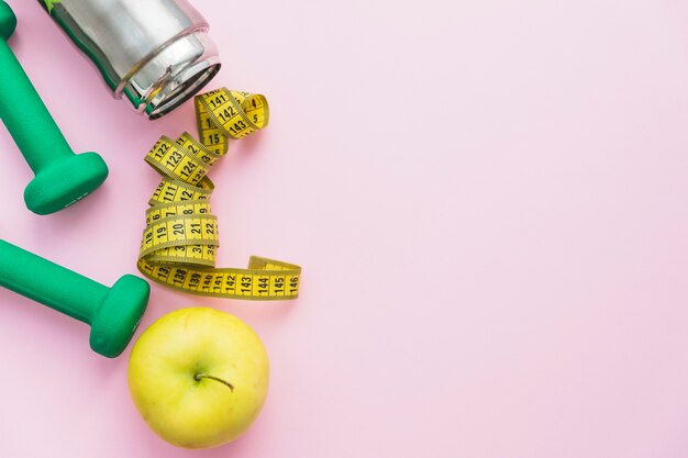 Hanteln; Wasserflasche; Maßband und Apfel auf rosa Hintergrund