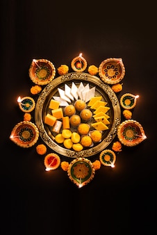Happy diwali - flower rangoli mit süßigkeiten oder mithai und diya in schalen für diwali oder andere feste in indien, selektiver fokus