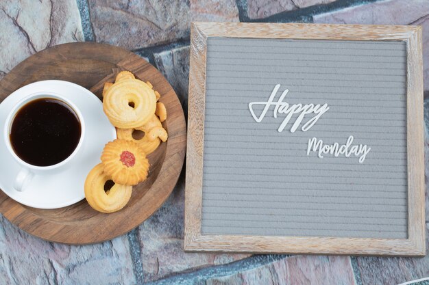 Happy Monday Poster eingebettet auf grauem Hintergrund mit einer Tasse Getränk und Keksen herum