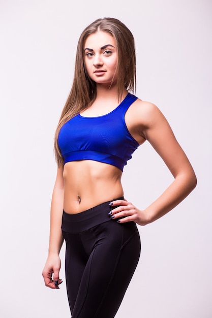 Harte junge Frau, die auf grauem Hintergrund steht. Weiblicher Bodybuilder, der Handschuhe trägt, die für Sportübung bereit sind.