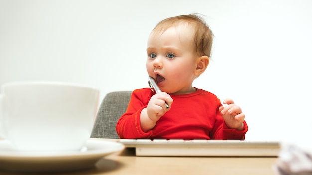 Harter Tag. Kindbaby, das mit Tastatur des modernen Computers oder des Laptops im weißen Studio sitzt