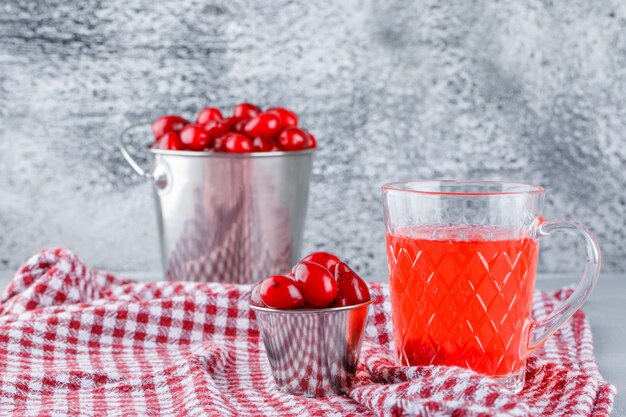 Hartriegelbeeren in Eimern mit Getränk, Picknickstoff-Seitenansicht auf Gips und grungy