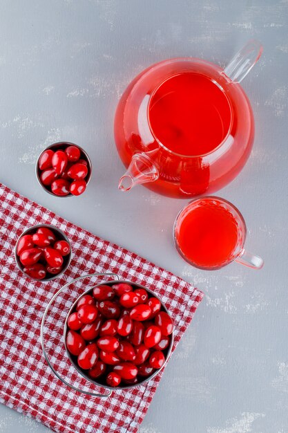 Hartriegelbeeren mit Getränk in Eimern auf Gips und Picknicktuch, Draufsicht.