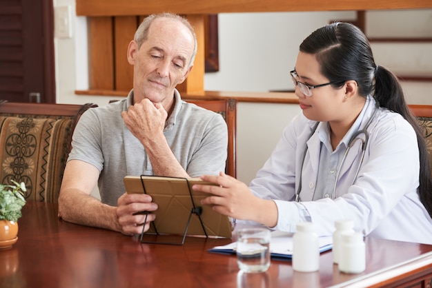 Hausarzt, der dem älteren Patienten Testergebnisse auf Tablet-PC zeigt