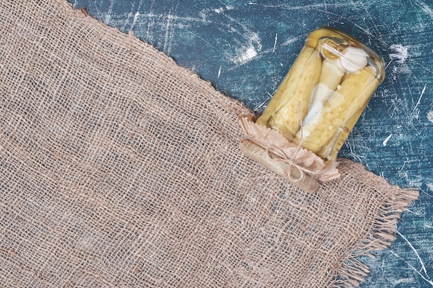 Hausgemachte eingelegte Gurken im Glas auf Blau mit Wolltischdecke.