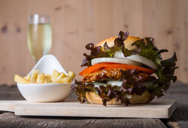 Hausgemachte Hähnchenburger mit Champagner, Pommes frites, Salat, Tomaten und Zwiebeln auf Holzbrett.