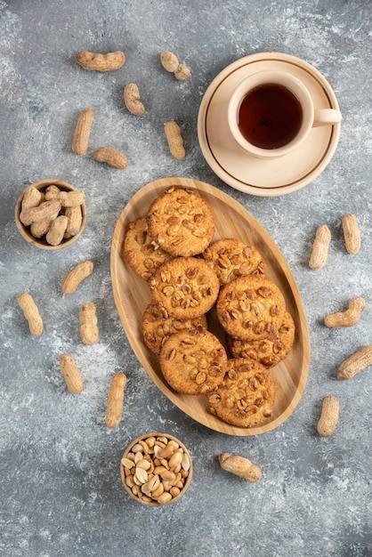 Hausgemachte Kekse mit Bio-Erdnüssen und Honig auf Holzbrett mit Tasse Tee.