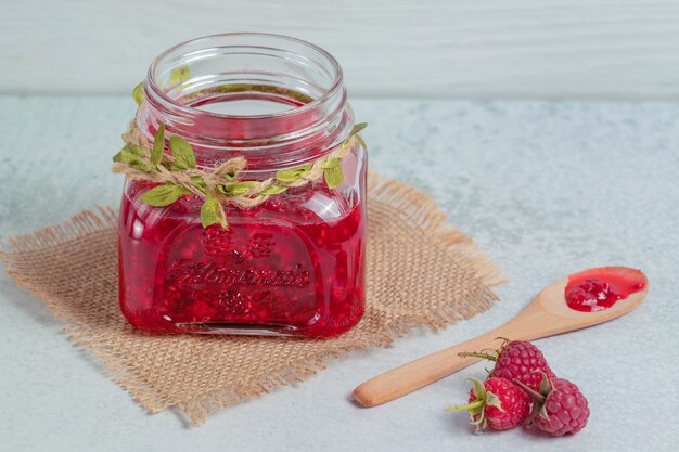 Hausgemachte Marmelade und frische Himbeeren auf grauer Oberfläche.