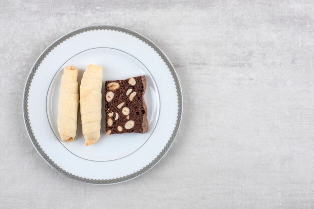 Hausgemachte Schokoladen-Brownies und Brötchen auf einem Teller, auf dem Marmortisch.