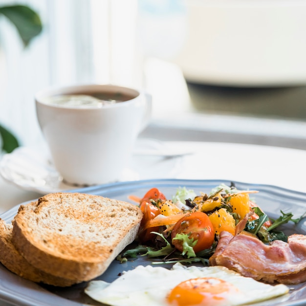 Kostenloses Foto hausgemachte spiegeleier; salat und speck auf teller vor kaffeetasse