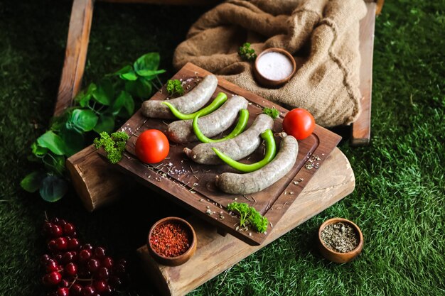 Hausgemachte Würste auf dem Holzbrett mit Fleisch Tomaten Tomaten Grün Salz Pfeffer Seitenansicht