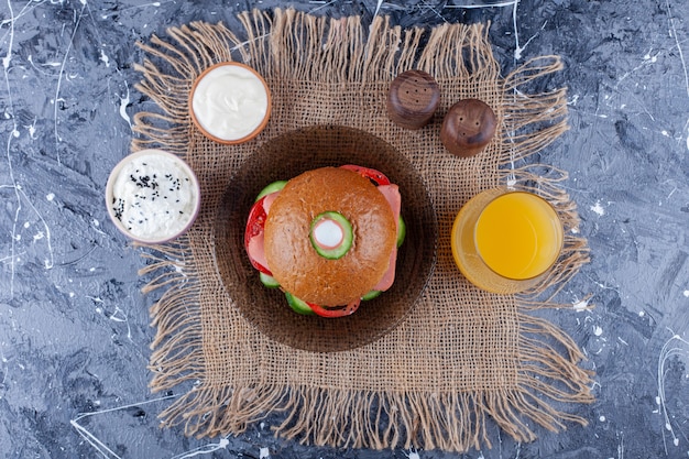 Hausgemachter Burger auf Teller neben einem Glas Saft auf Leinenserviette auf Blau.