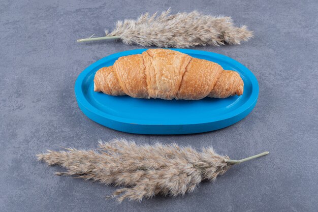 Hausgemachtes frisches Croissant auf blauem Holzbrett.