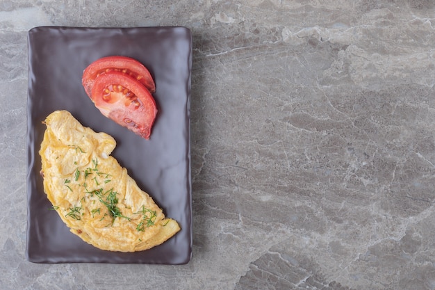 Hausgemachtes leckeres Omelett mit Tomate auf dunklem Teller.