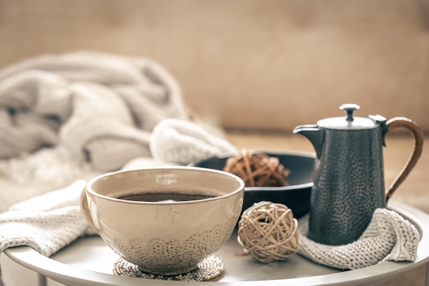 Hauskomposition mit einer Tasse Tee und einer Teekanne auf einem verschwommenen Hintergrund