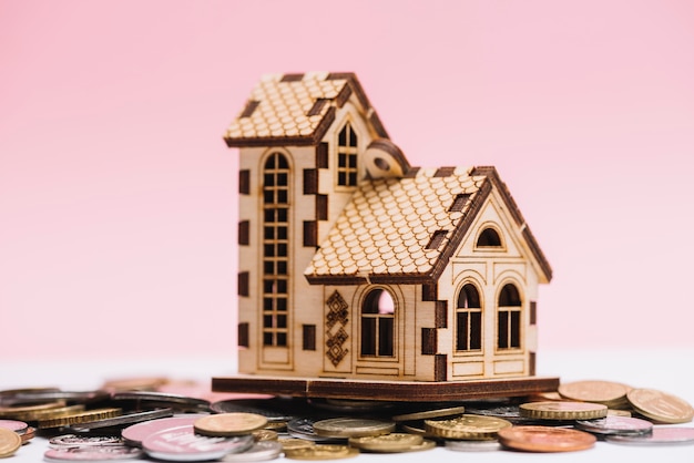 Hausmodell über münzen vor rosa hintergrund