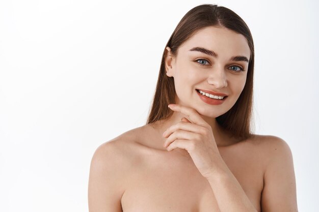 Hautpflege nach der Wirkung. Lächelnde junge Frau mit gesunder, hydratisierter und mit Feuchtigkeit versorgter natürlicher Haut, die das Gesicht in der Nähe des Kiefers berührt und zufrieden aussieht, kosmetische Behandlung von Akne und Hautunreinheiten, reine Poren