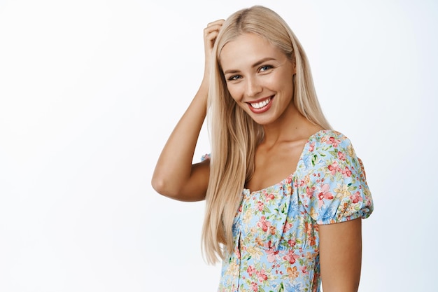 Hautpflege und Schönheit Schönes blondes Mädchen, das die Kamera anstarrt, die flirty im Kleid gegen weißen Hintergrund stehend lächelt