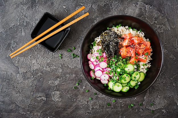 Hawaiian Lachs Fisch Poke Bowl mit Reis, Radieschen, Gurke, Tomate, Sesam und Seetang. Buddha-Schale. Diätessen. Draufsicht. Flach liegen