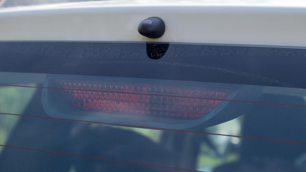 Heckscheibe eines staubigen weißen autos mit einer ampel hinter glas, nahaufnahme. rote signale, die das bremsen des fahrzeugs anzeigen. sie schalten sich automatisch ein, wenn sie die bremse betätigen und schalten sich aus, wenn sie sie loslassen.