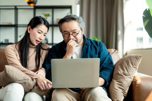 Heiraten Sie ein asiatisches Paar, das die Haushaltsfinanzen überprüft, die ihre Bankgeldkonten mit einem Laptop und einem Taschenrechner im Wohnzimmer überprüfen