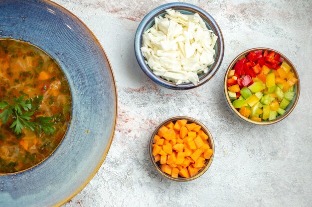 Heiße Gemüsesuppe der Draufsicht mit geschnittenem Gemüse auf weißem Raum