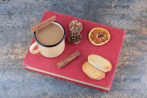 Heiße Tasse Kaffee mit Zimtstange und Keksen auf Buch. Foto in hoher Qualität